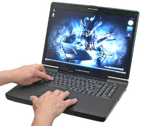 Hands typing on Alienware Area-51 m9750 laptop with graphic wallpaper.