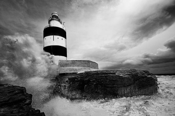 Black and white photo of a lighthouse with crashing waves.