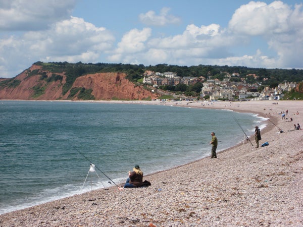 Beach landscape with people fishing and red cliffs.