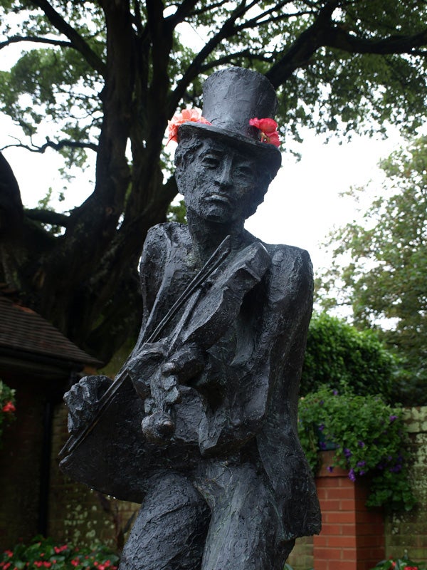 Bronze statue of a musician with a top hat and flowers.
