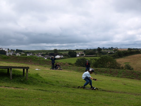 Photograph of person riding a mountain board on grassy hill.