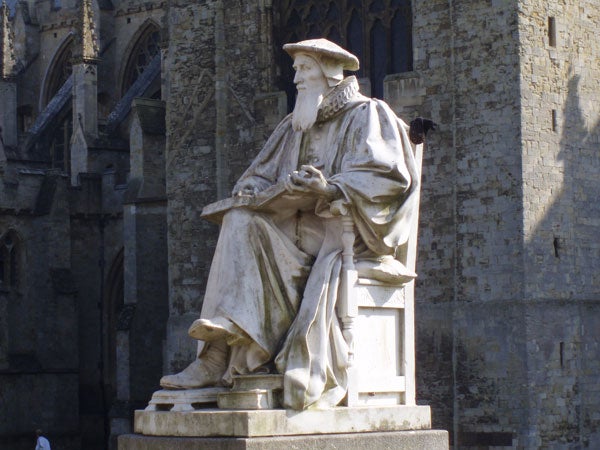 Statue of a seated historical figure against a cathedral backdrop.