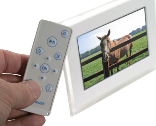 Hand holding Momento i-mate 100 remote with digital frame displaying horse.