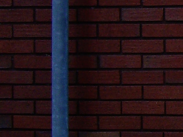 Blurred photo of a pole against a brick wall.