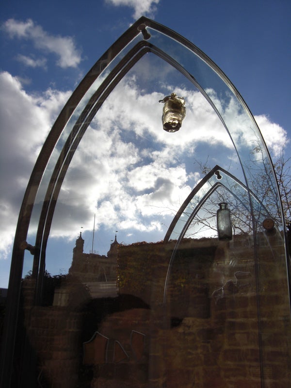 Reflective glass sculpture against a blue sky with clouds.Glass art installation with floating jars and blue sky.