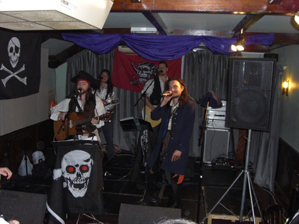 Band performing in pirate costumes at a themed eventPirate-themed band performing on stage with musical instruments.