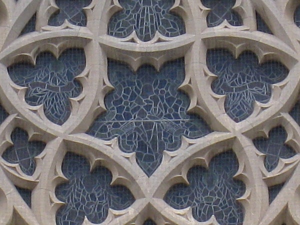 Stone building with intricate gothic window tracery.Close-up of intricate stone carving patterns on a wall.
