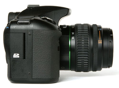 Pentax K10D Digital SLR camera with lens viewed from the side.Pentax K10D DSLR camera with lens on white background.