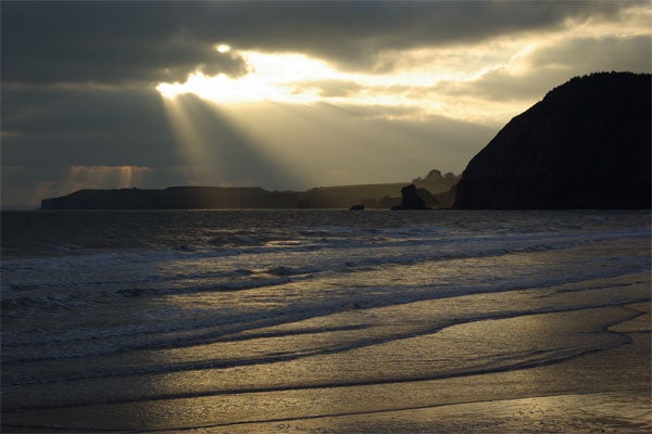Sun rays piercing through clouds over a serene coastline.Sun rays piercing through clouds over a scenic coastline.