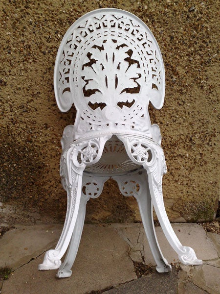 Ornate white metal garden chair against concrete wall.Ornate white cast iron garden chair against a wall.