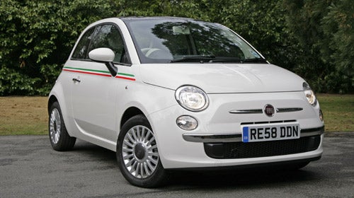 White Fiat 500 parked outdoors with trees in the background.