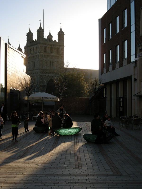 Outdoor photo showing a plaza with people and historic tower at dusk.