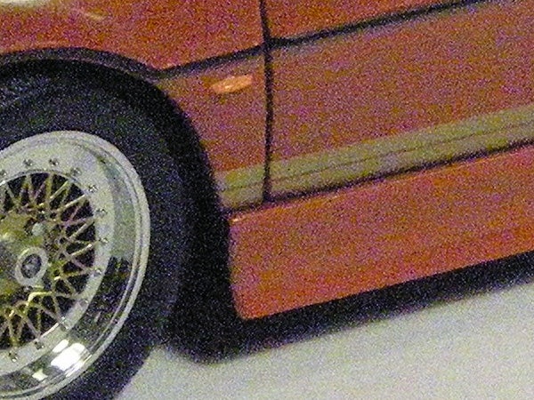 Close-up of car wheel and side panel with noise artifacts.