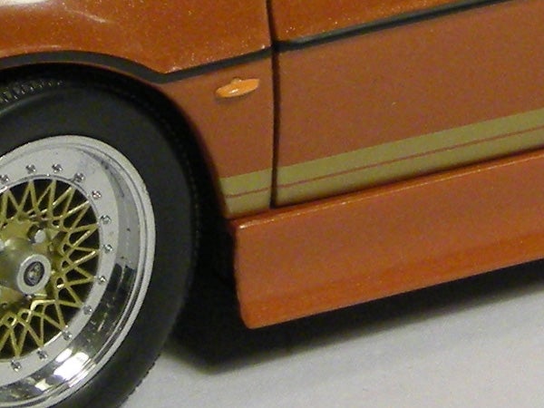 Close-up of orange car model's wheel and side panel.