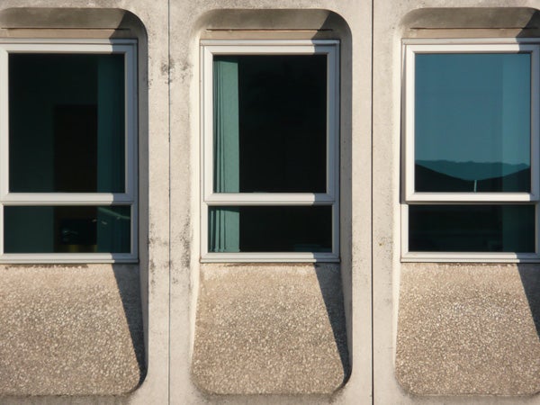 Three windows on a building facade with mountain view.