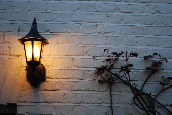 Illuminated lantern on a brick wall at dusk.Warmly lit outdoor lantern on a white brick wall at dusk.