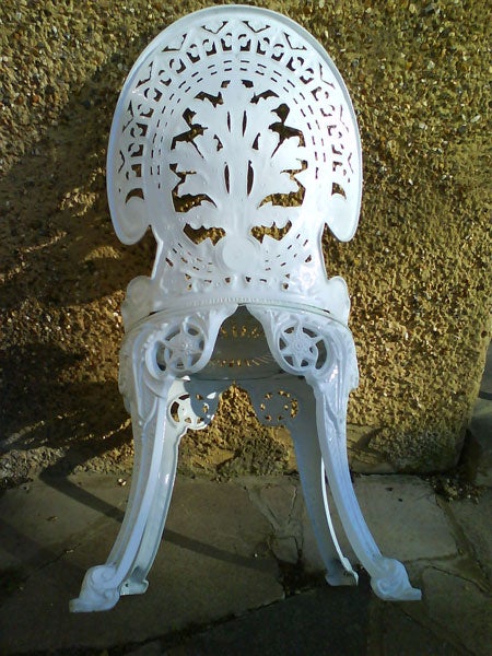 White ornate cast iron chair outsideWhite ornate cast iron chair against a wall.