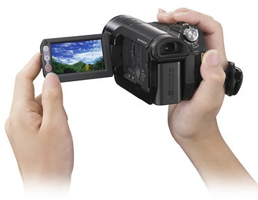Hands holding Sony HDR-HC9E camcorder with display screen open.Hands holding a Sony HDR-HC9E HDV camcorder with LCD screen open.