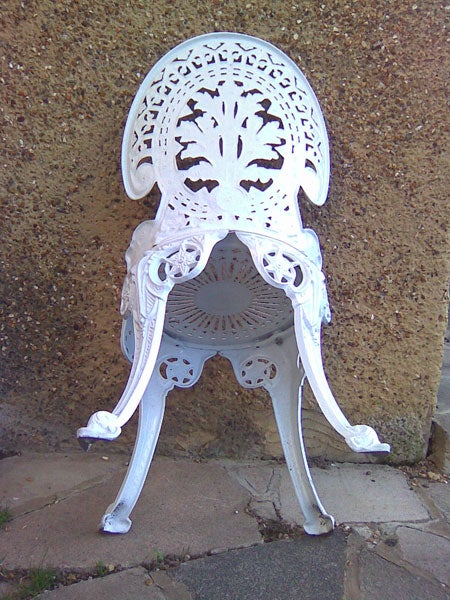 White ornate metal chair against a wall.