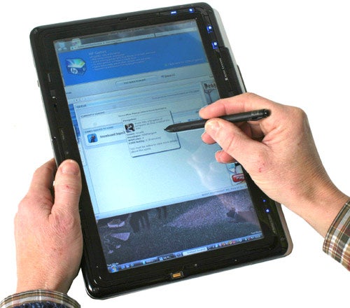Hands holding HP Pavilion tx2050ea in tablet mode with stylus.HP Pavilion tx2050ea laptop in tablet mode with stylus.