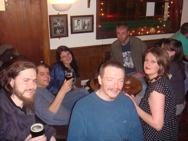 Group of people socializing in a pub, one holding a camera.Group of people smiling in a pub, one holding a camera.