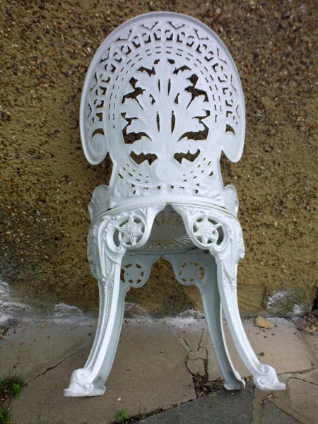 White ornate metal garden chair against a wall.