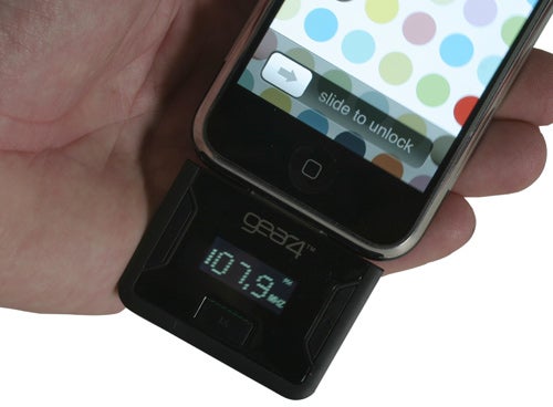 Hand holding iPhone with Gear4 AirZone FM Dock displaying frequency.