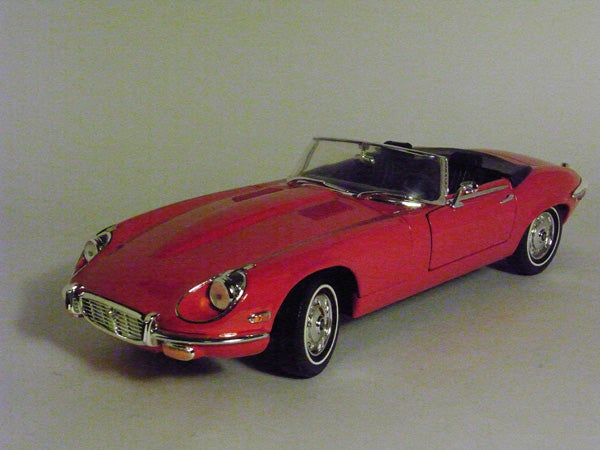 Red toy model of a classic convertible car on a gray surface.Red Jaguar E-Type convertible model car on a gray background.