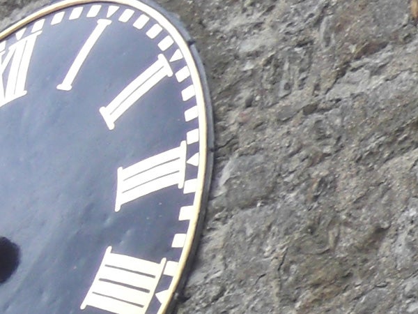Close-up of a clock face with Roman numerals against stone.image of a clock face against a rock background