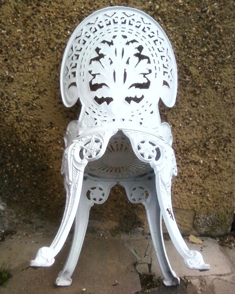 Ornate white metal chair against a concrete wall.White ornate plastic chair against a wall.