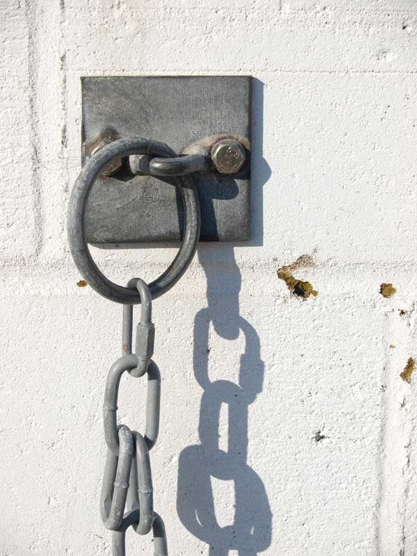 Metal ring and shadow on a white wall.Metal ring and chain attached to a white wall in sunlight.