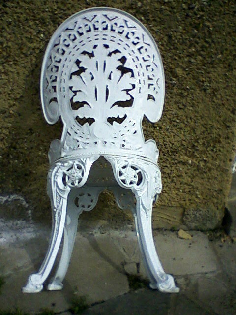 White ornate cast iron garden chair against a wall.Intricately designed white metal garden chair against a wall