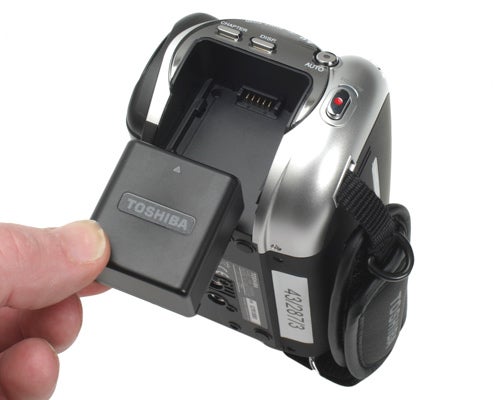 Toshiba Gigashot A100FE camcorder with open battery compartment.Hand holding Toshiba Gigashot A100FE with open battery compartment.