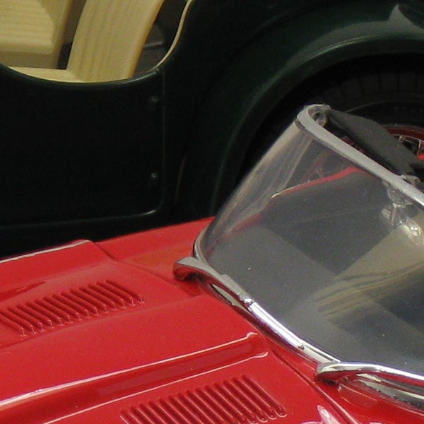 Close-up of a red toy car next to another vehicle.Close-up of a red classic car model's hood and windshield.