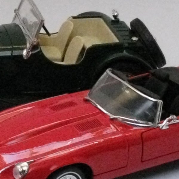 Diecast model cars on display, red in front, black behind.Close-up of toy cars with a focus on the red convertible.