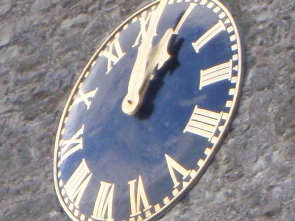 Close-up of a sundial showing the time as approximately 1:50.Oval clock face with roman numerals on stone background.