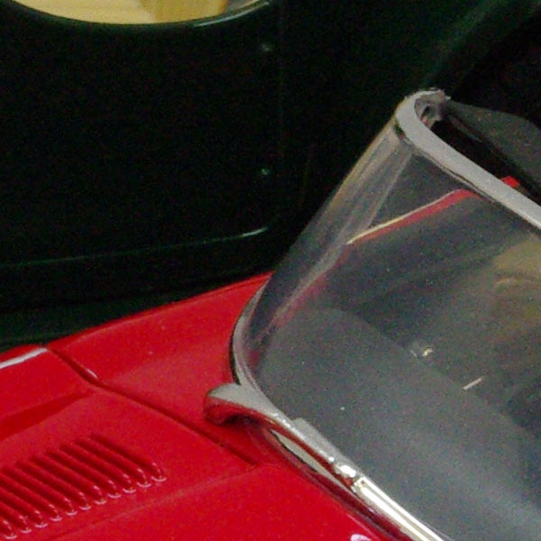 Close-up of red car with clear headlight cover.Close-up of a red toy car and black mug on a desk.