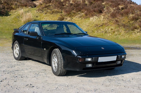 Black sports car parked on gravel with grassy background.Black sports car parked on gravel with a grassy hill behind.