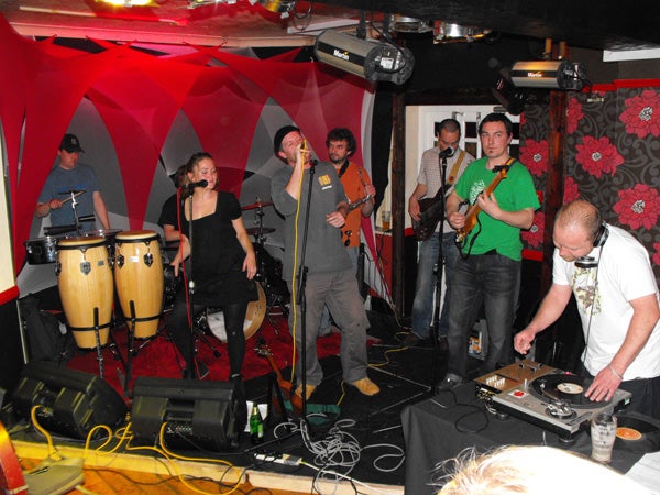 Band performing on stage with colorful background and DJ booth.Band performing on stage in a small club setting.