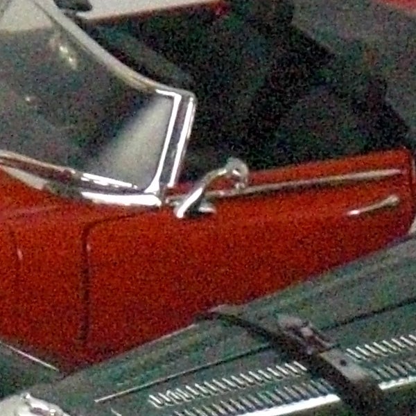 Close-up of a car's side panel and door handleGrainy photo of a vintage red car on display