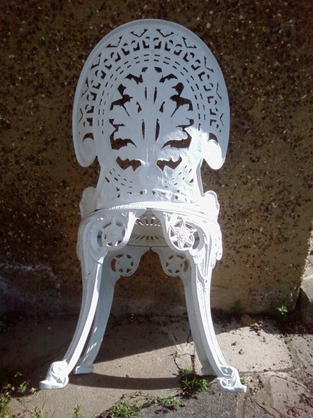 White ornate metal garden chair against a wall.White ornate garden chair against a concrete wall.