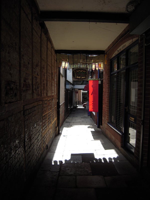 Narrow alleyway with sun casting shadows on pavement.Narrow alley with sun casting shadows, bright contrast.