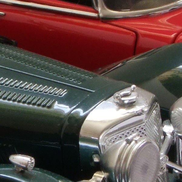 Close-up of a vintage camera with classic cars in background.Fujifilm FinePix S100FS camera close-up with cars.