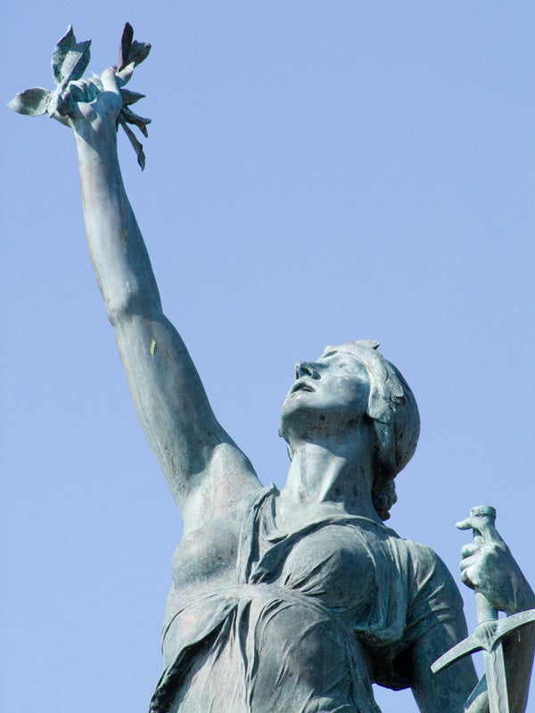 Statue of a woman with raised arm holding doves against sky.Bronze statue holding aloft a dove against blue sky.
