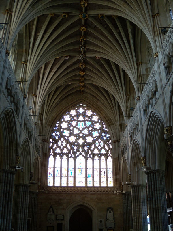 Gothic cathedral interior with vaulted ceiling and stained glass window.