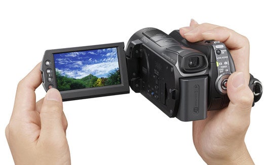 Hands holding Sony HDR-SR12E camcorder with landscape on display.