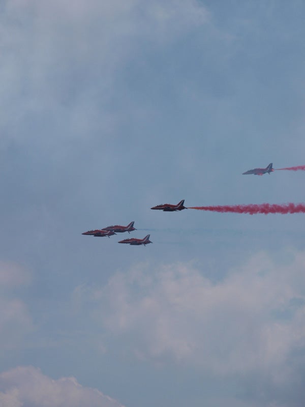 Jets performing aerial maneuvers with red smoke trailsJets flying with red smoke trails against a cloudy sky.