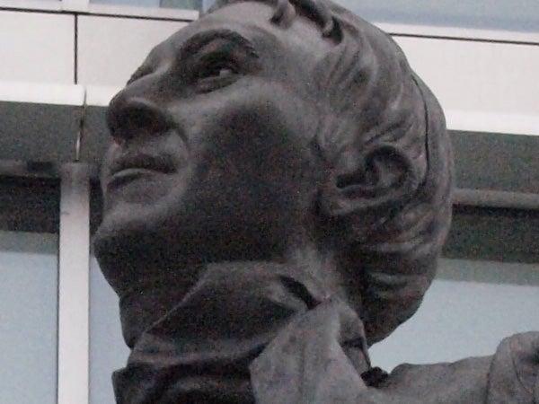 Close-up of a bronze statue of a man's face.Close-up of a bronze statue's face against a building.