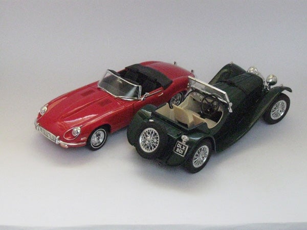 Two model cars captured in sharp detail by camera.Model toy cars, a red and a green convertible, photographed on a white background.