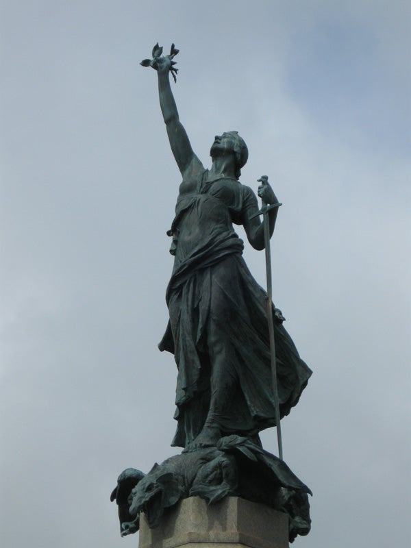Statue of a figure holding a bird and staff against the sky.